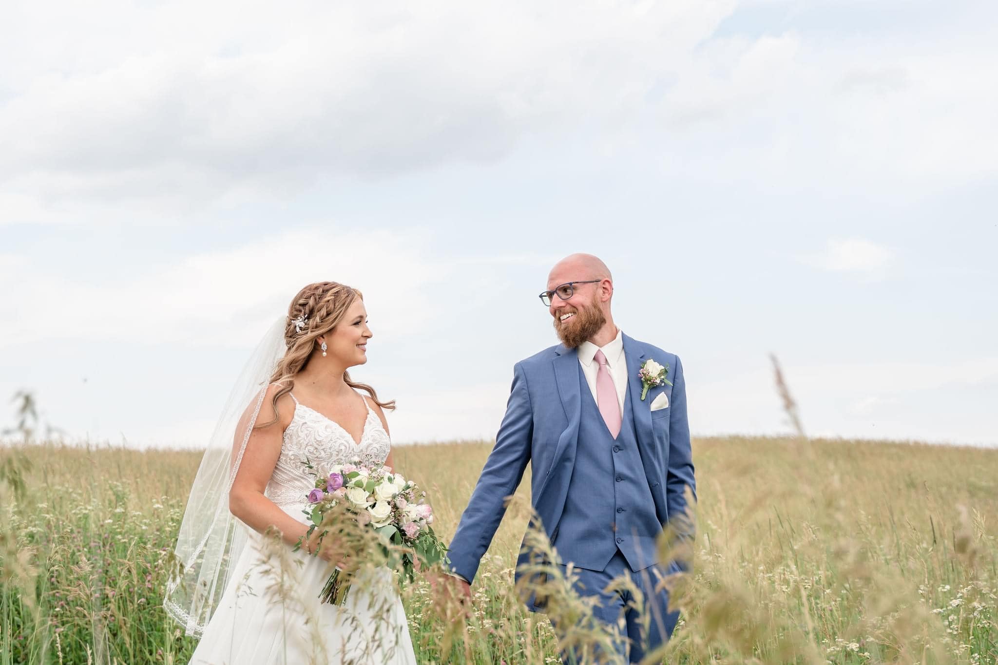 bride and groom holding hands and walking through green field