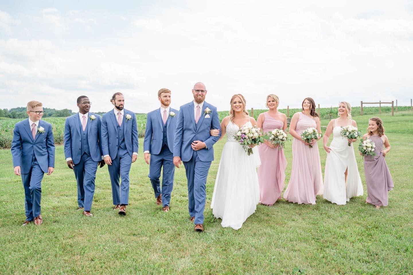 couple with wedding party walking through green field