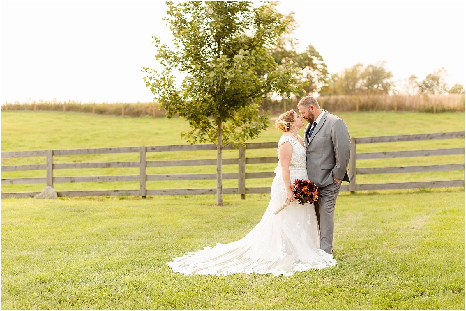 bride and groom kissing in front of wooden fence in green field